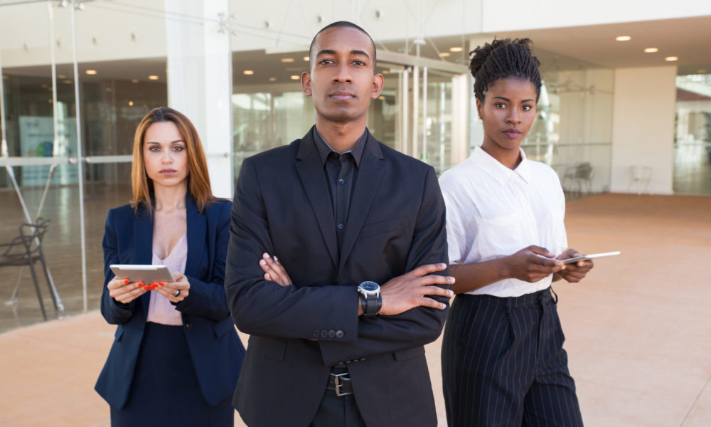 Successful business team posing in office hall Successful business team posing in office hall. Three mix raced professionals with arms crossed standing in office hall and looking at camera. Multiethnic business team concept